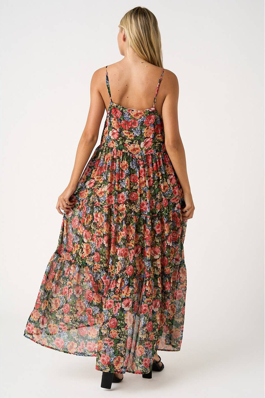 Back view of a woman wearing a floral tiered maxi dress on a white background