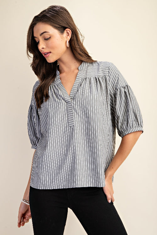 Woman wearing a striped navy and white blouse with puff sleeves on a beige background