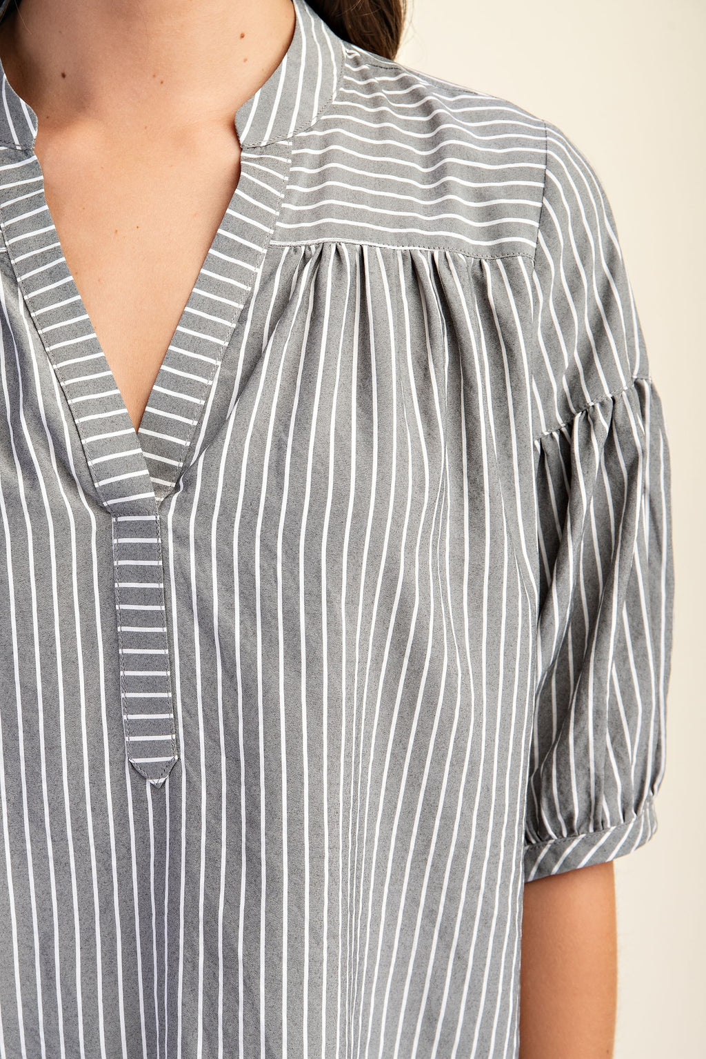 Woman wearing a striped navy and white blouse with puff sleeves on a beige background