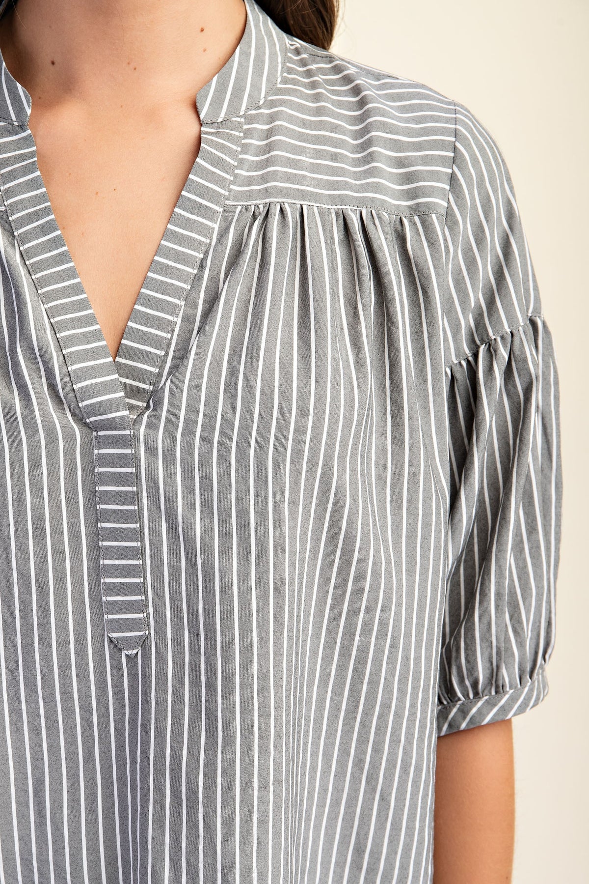 Woman wearing a striped navy and white blouse with puff sleeves on a beige background
