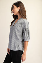 Woman wearing a striped navy and white blouse with puff sleeves on a beige background