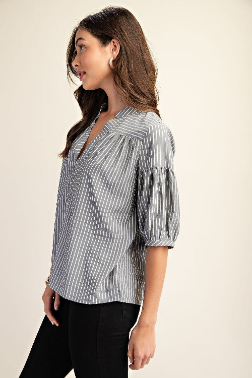 Woman wearing a striped navy and white blouse with puff sleeves on a beige background