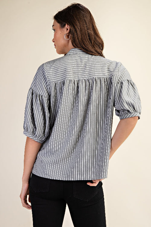 Back view of a woman wearing a striped navy and white blouse with puff sleeves on a beige background