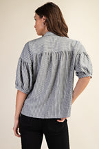 Back view of a woman wearing a striped navy and white blouse with puff sleeves on a beige background