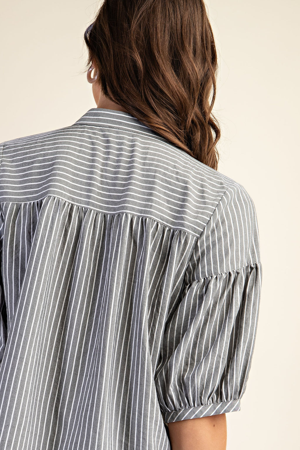 Back view of a woman wearing a striped navy and white blouse with puff sleeves on a beige background