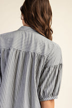 Back view of a woman wearing a striped navy and white blouse with puff sleeves on a beige background
