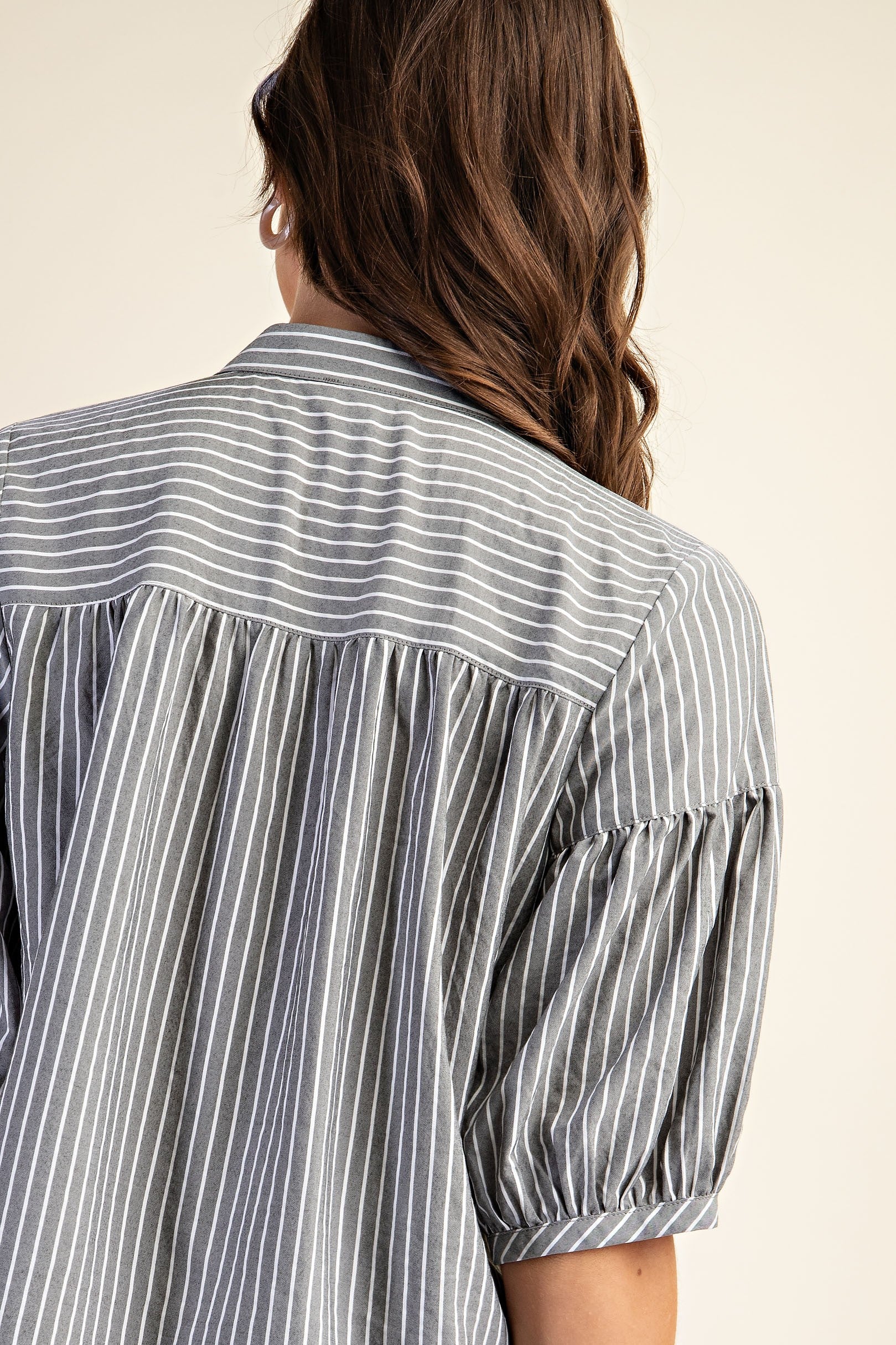 Back view of a woman wearing a striped navy and white blouse with puff sleeves on a beige background