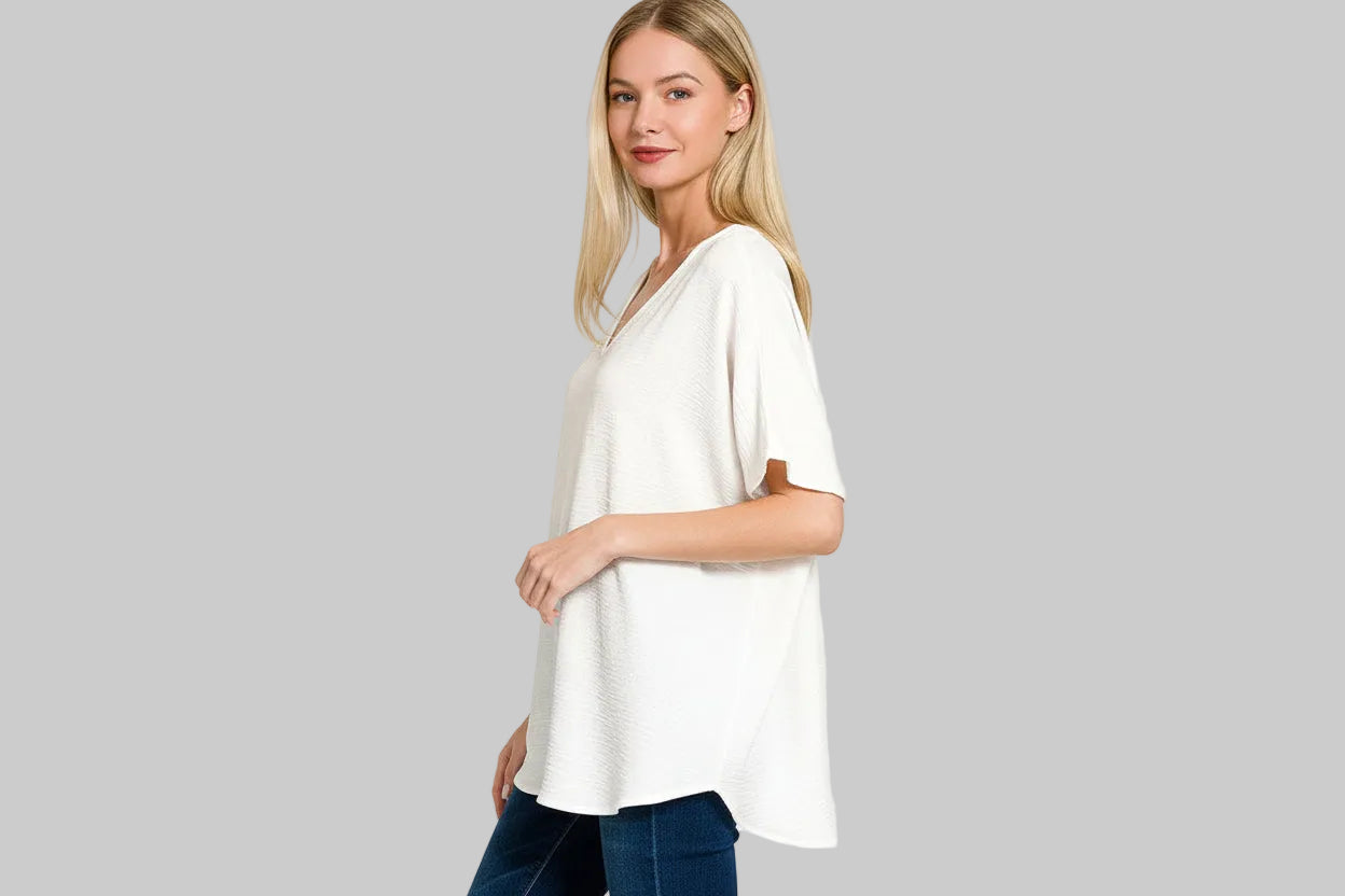 Woman wearing a white blouse with a V-neck and short sleeves on a grey background