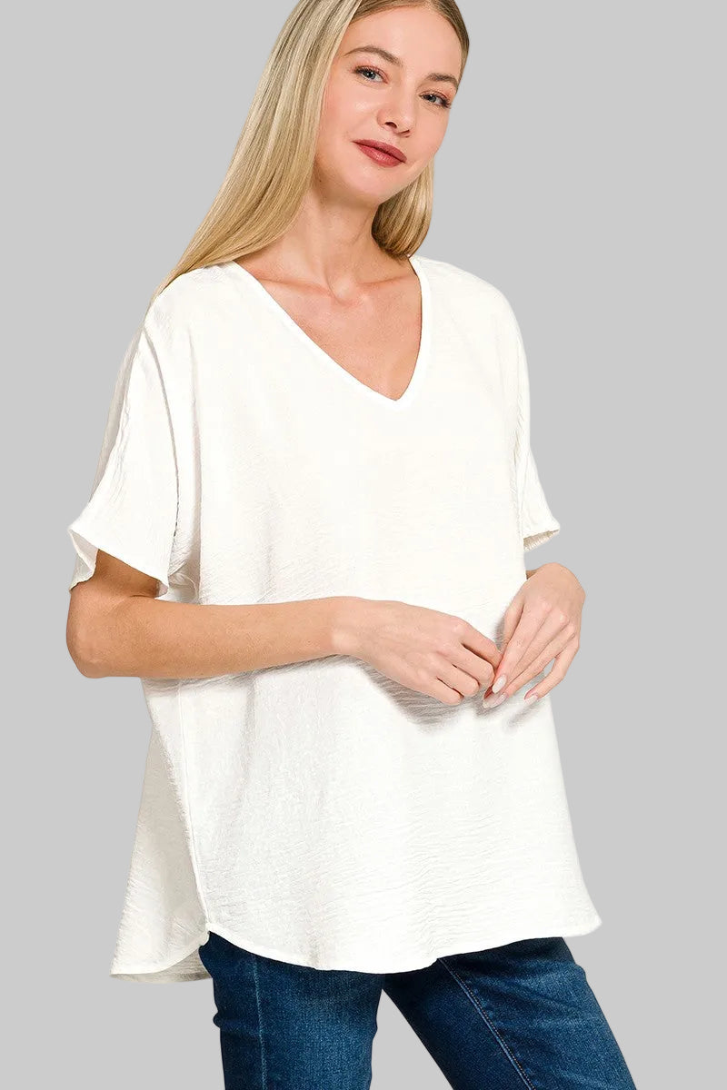 Woman wearing a white blouse with a V-neck and short sleeves on a grey background