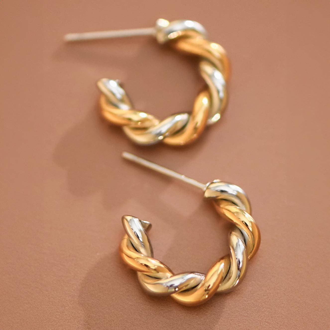 Pair of gold and silver twisted hoop earrings on a beige background