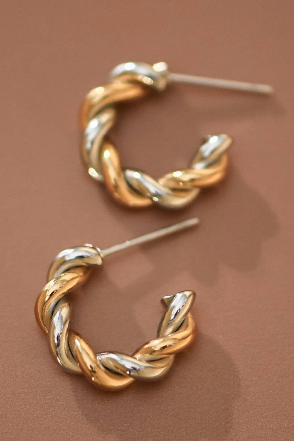 Pair of gold and silver twisted hoop earrings on a beige background