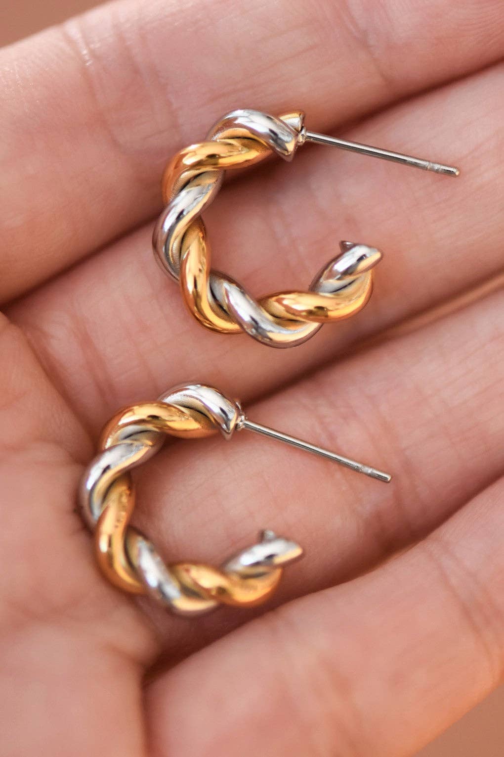 Pair of gold and silver twisted hoop earrings held in a hand.