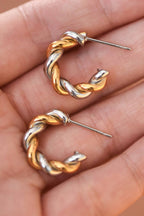 Pair of gold and silver twisted hoop earrings held in a hand.