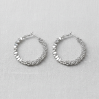 Pair of silver hoop earrings with texture on a light gray background