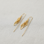 Gold leaf-shaped threader earrings on a light gray fabric background