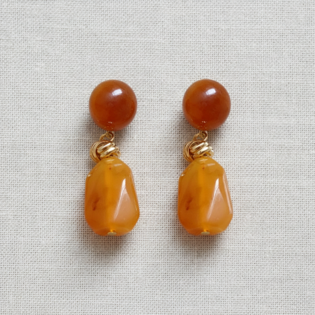 Pair of earrings with brown and gold stone look on a light gray background