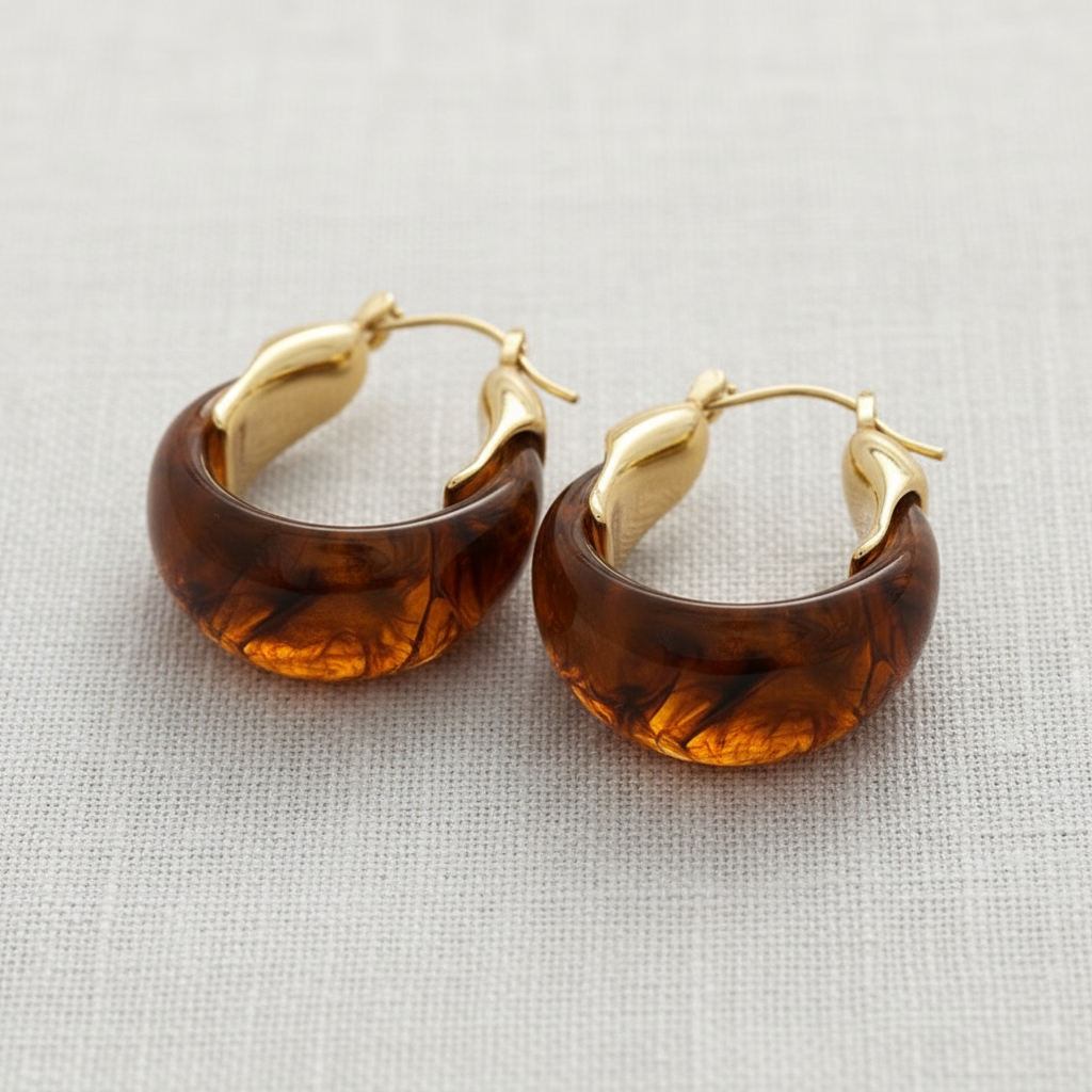 Pair of brown hoop earrings with gold accents on a light gray fabric background