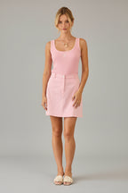 Woman wearing a pink tank top and skirt standing in a room with beige walls and curtains.