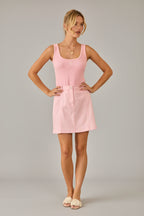 Woman wearing a pink tank top and skirt standing in a room with beige walls and curtains.