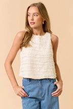 Woman wearing a sleeveless ruffle top in cream and jeans on beige background