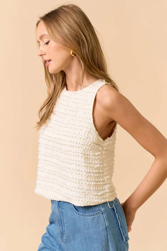 Woman wearing a sleeveless ruffle top in cream and jeans on beige background