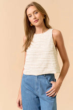 Woman wearing a sleeveless ruffle top in cream and jeans on beige background
