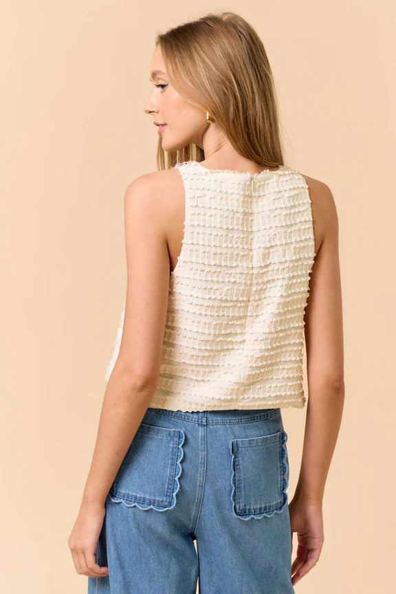 Back view of a woman wearing a sleeveless ruffle top in cream and jeans on beige background