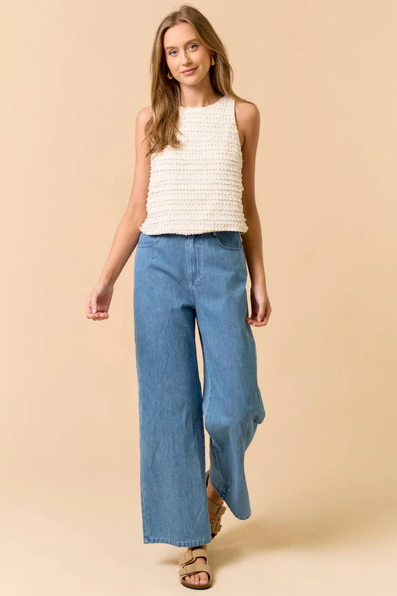 Woman wearing a sleeveless ruffle top in cream and jeans on beige background