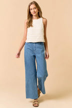 Woman wearing a sleeveless ruffle top in cream and jeans on beige background