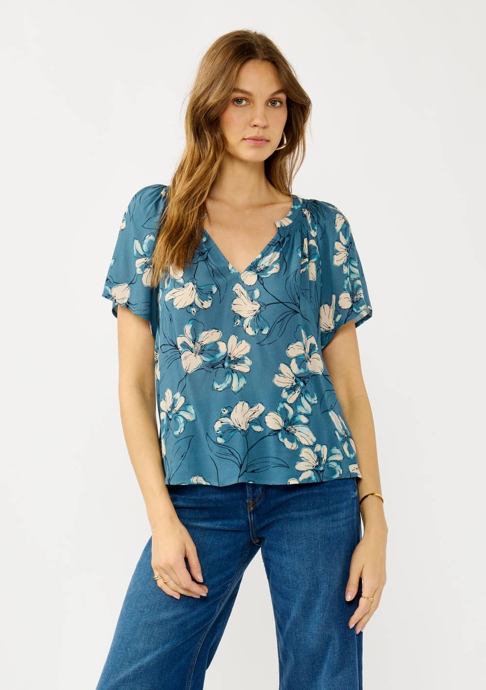 Woman wearing a teal blue floral blouse and jeans on a white background