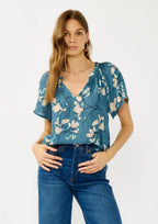 Woman wearing a teal blue floral blouse and jeans on a white background