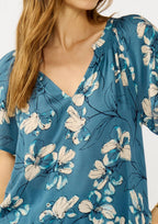 Woman wearing a teal blue floral blouse and jeans on a white background