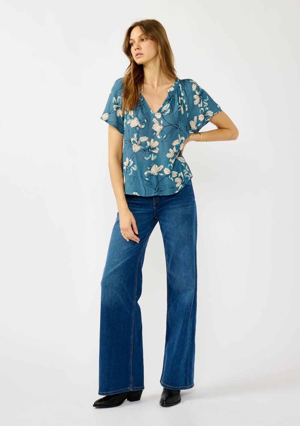 Woman wearing a teal blue floral blouse and jeans on a white background