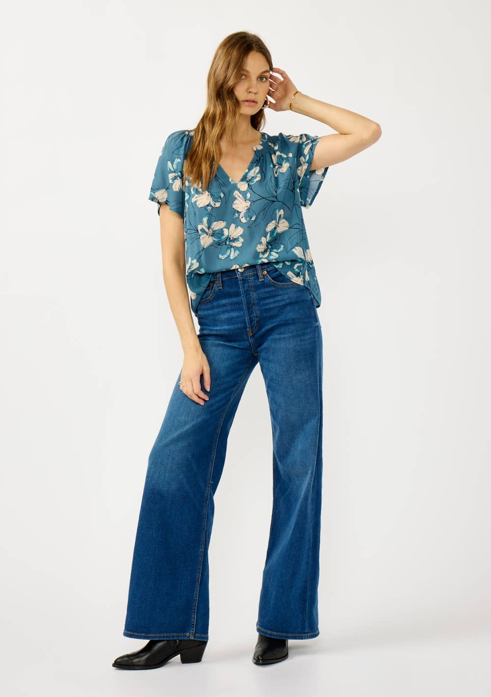 Woman wearing a teal blue floral blouse and jeans on a white background