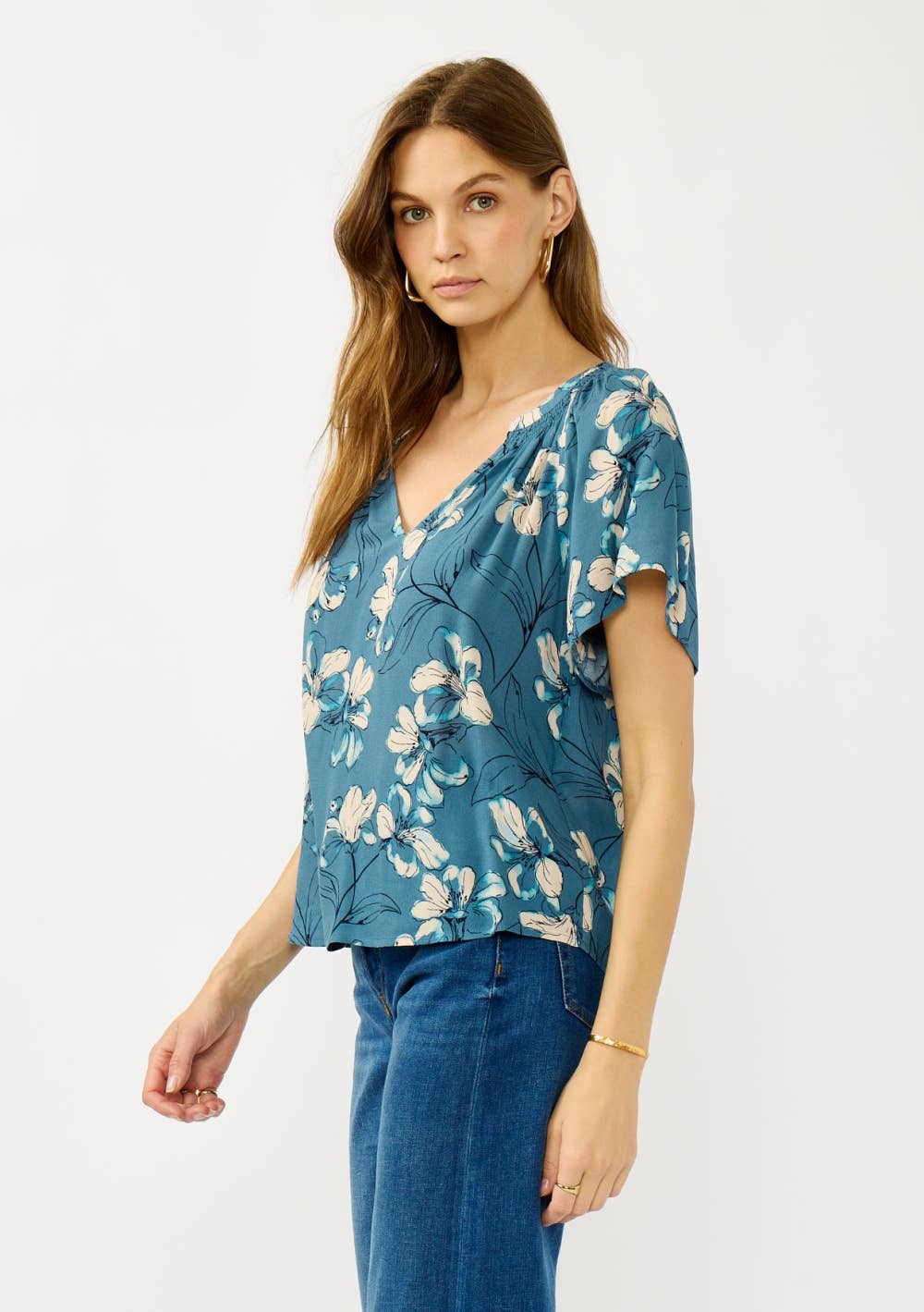 Woman wearing a teal blue floral blouse and jeans on a white background