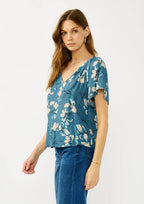 Woman wearing a teal blue floral blouse and jeans on a white background