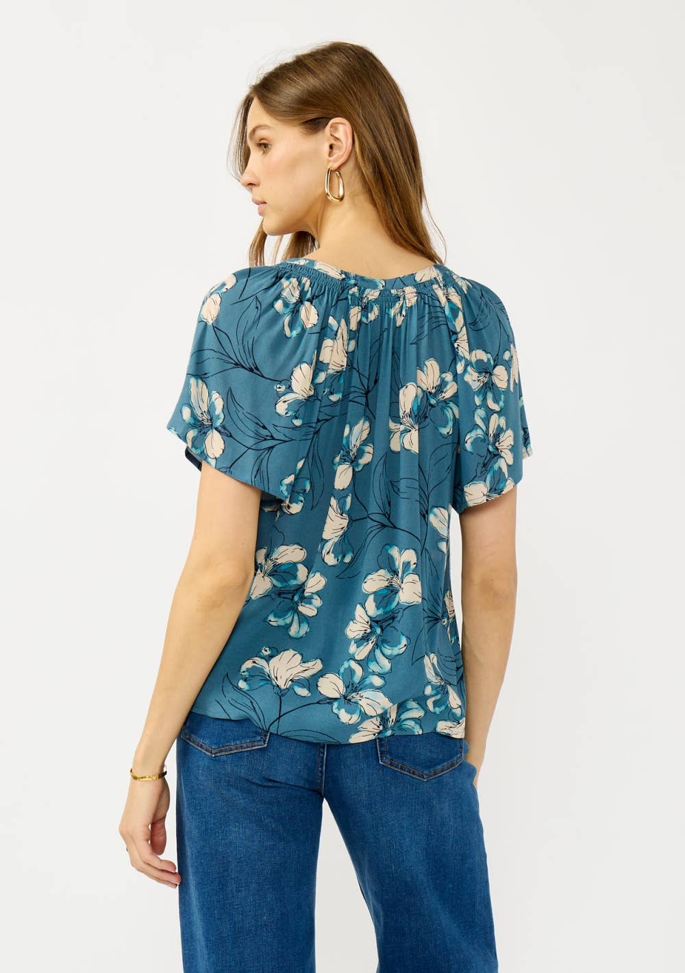 Woman wearing a teal blue floral blouse and jeans on a white background
