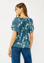 Woman wearing a teal blue floral blouse and jeans on a white background