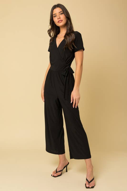 Woman wearing a black cropped jumpsuit against a beige background