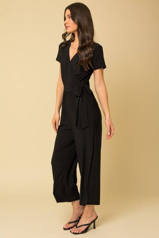 Woman wearing a black cropped jumpsuit against a beige background