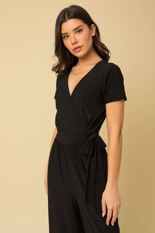 Woman wearing a black cropped jumpsuit against a beige background