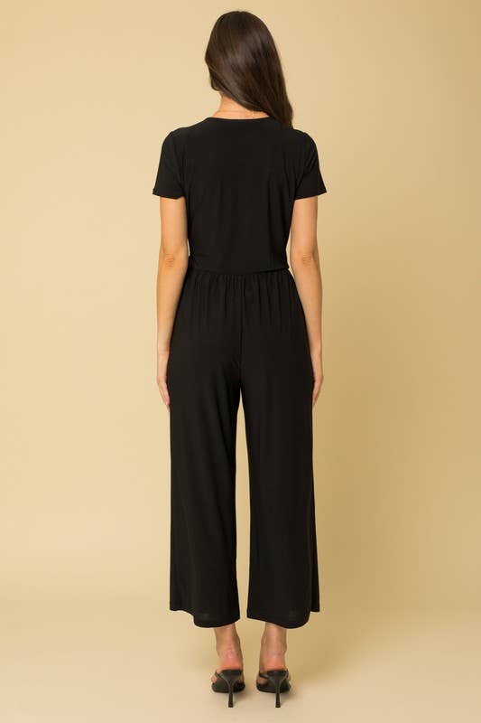 Back view of a woman wearing a black cropped jumpsuit against a beige background