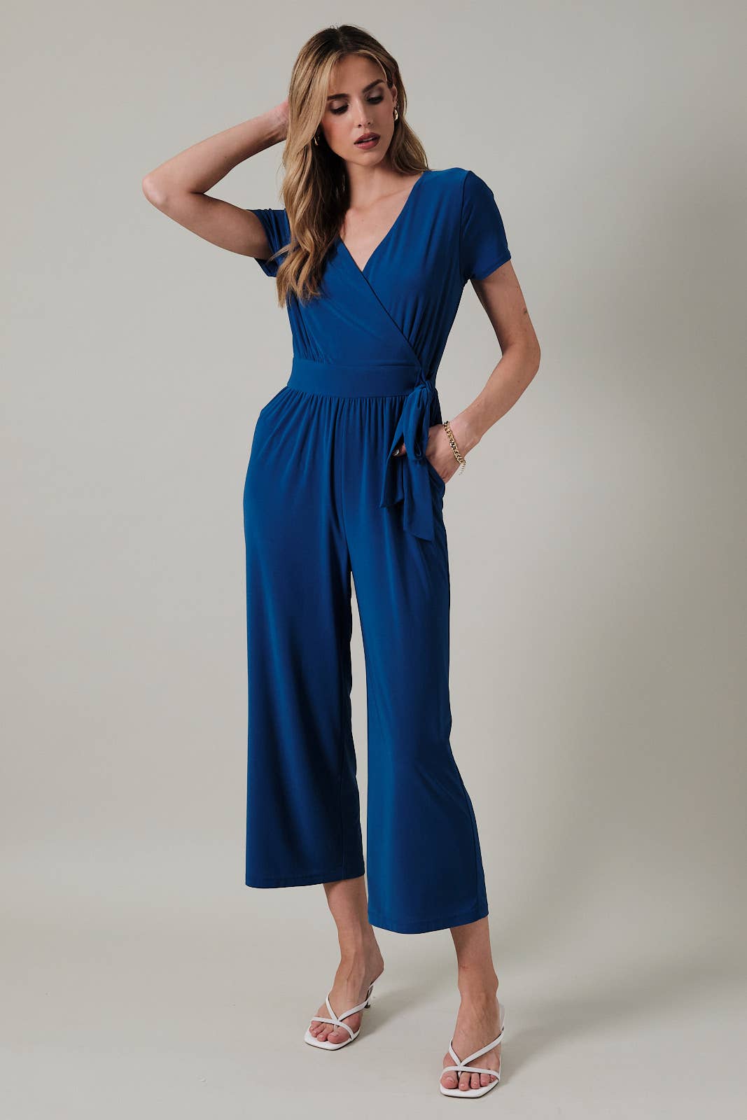 Woman wearing a royal blue faux wrap jumpsuit against a neutral background