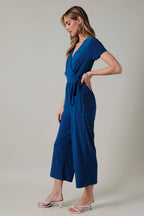 Woman wearing a royal blue faux wrap jumpsuit against a neutral background