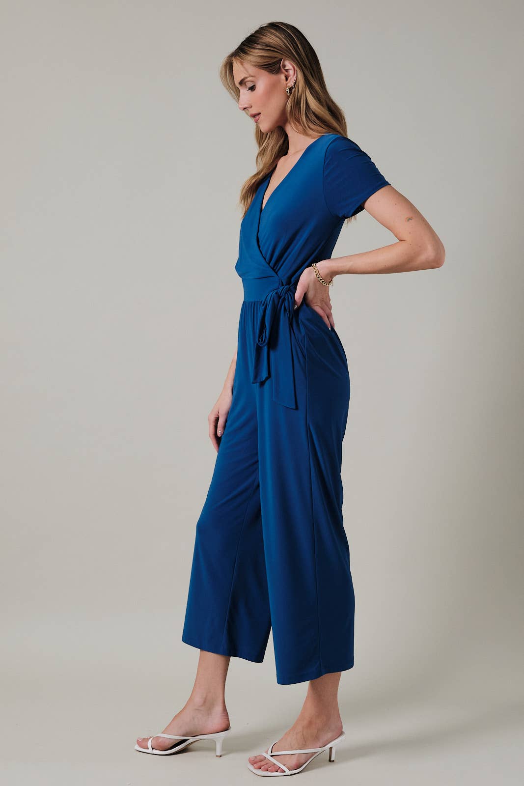 Woman wearing a royal blue faux wrap jumpsuit against a neutral background