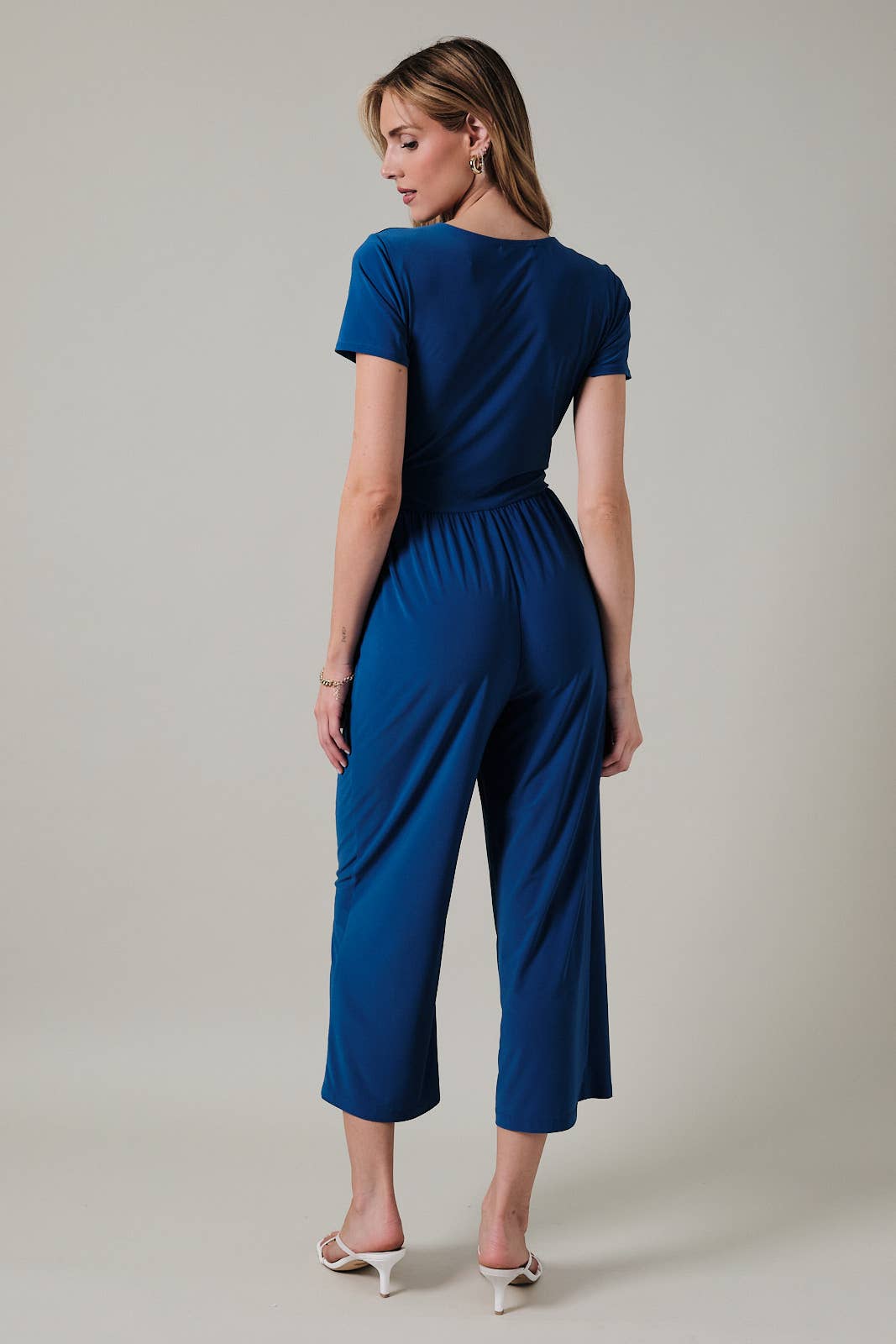 Back view of a woman wearing a royal blue faux wrap jumpsuit against a neutral background