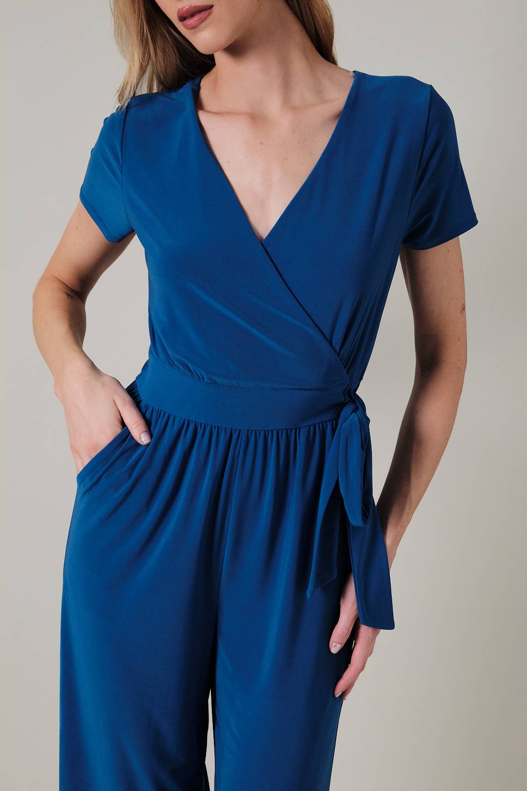 Woman wearing a royal blue faux wrap jumpsuit against a neutral background