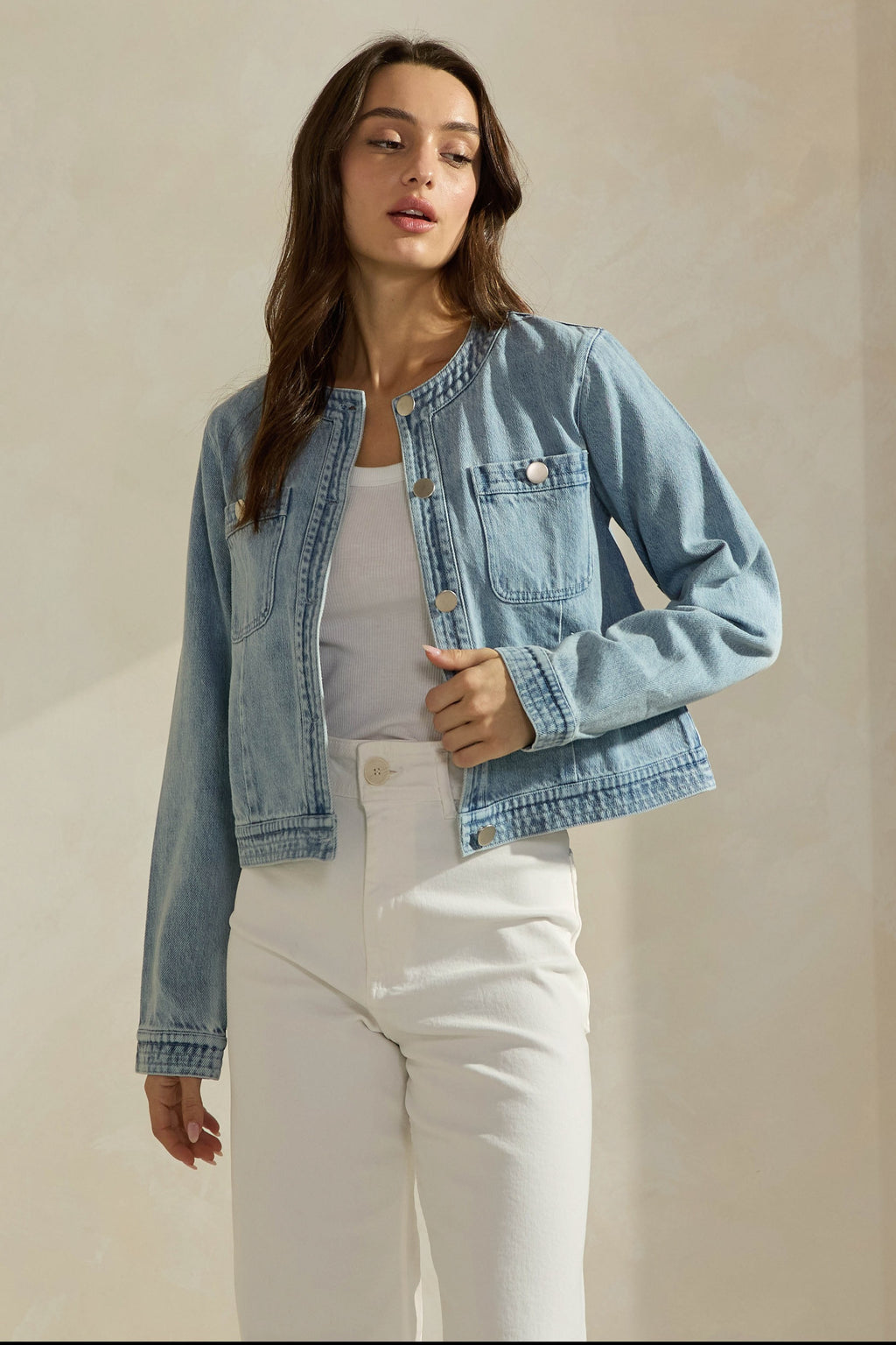 Woman wearing a light washed denim jean jacket on a neutral background