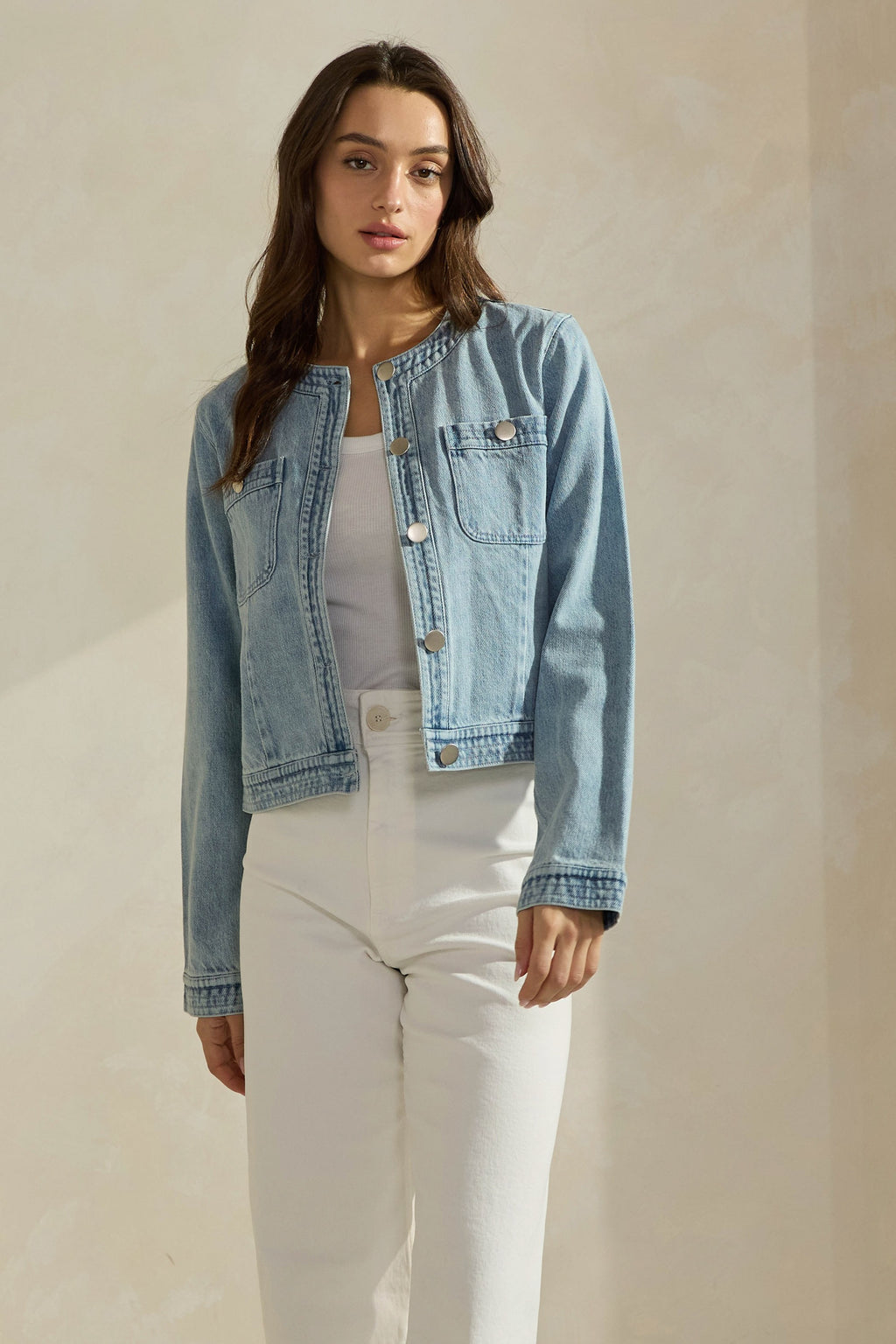 Woman wearing a light washed denim jean jacket on a neutral background