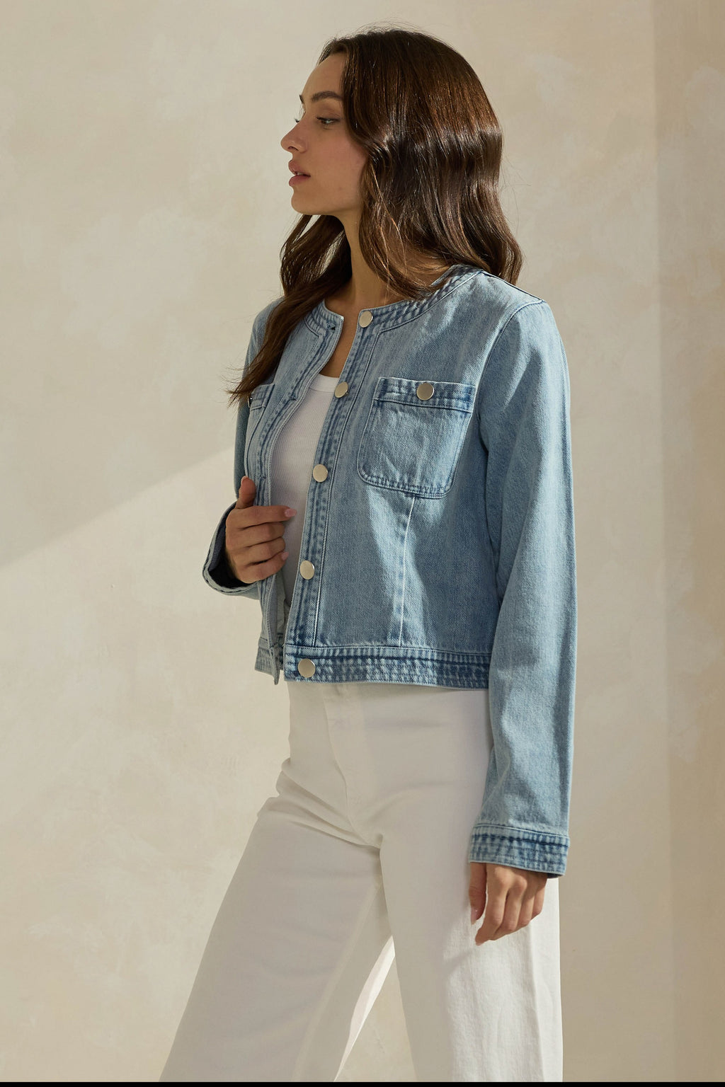 Woman wearing a light washed denim jean jacket on a neutral background